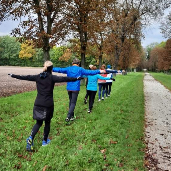 Alphalauf-Gruppe beim meditativen Laufen mit geöffneten Armen im Park